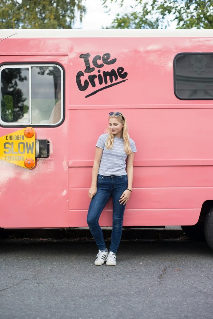 A girl in a striped shirt and jeans leans against a pink "Ice Crime" truck.